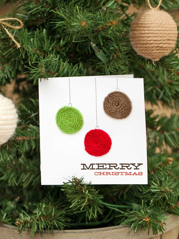 Nagyon ötletes megoldás, ha a karácsonyfa díszeket ragasztunk a készülő képeslapunkra. Ezt különböző színű fonalakból meg is oldható.
