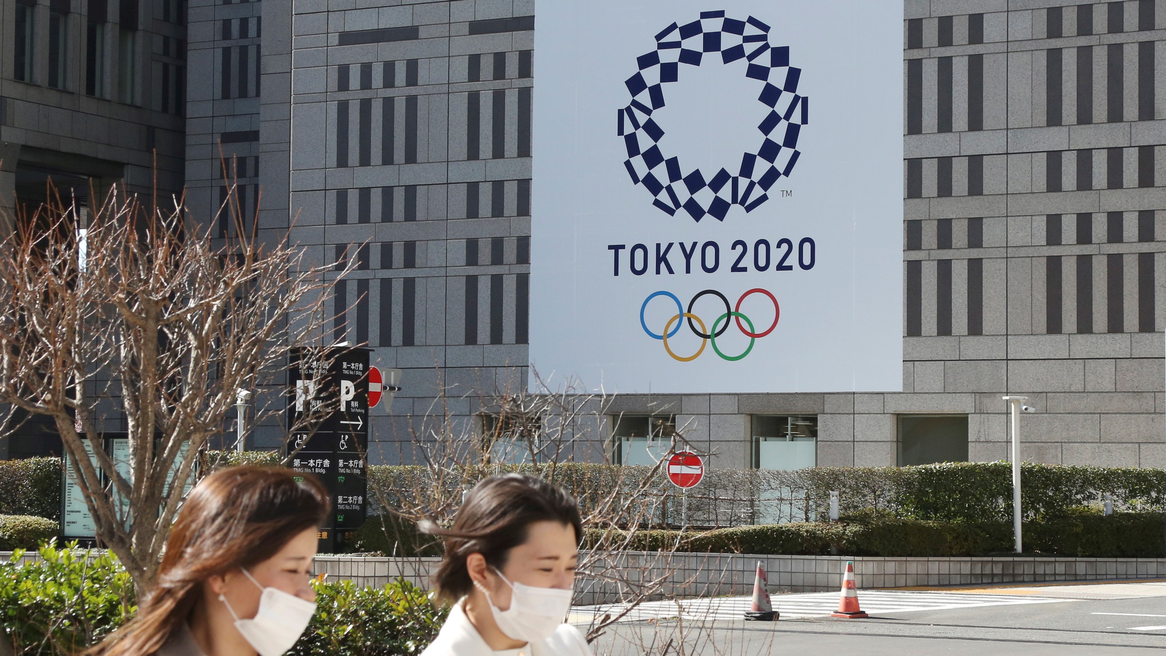 Két védőmaszkos nő megy a tokiói nyári olimpiát hirdető plakát előtt a japán fővárosban 2021. február 17-én. A koronavírus-járvány miatt 2020-ról 2021-re halasztott ötkarikás játékokat a tervek szerint 2021. július 23. és augusztus 8. között rendezik meg, de a legfrissebb közvéleménykutatások szerint a lakosság 80 százaléka vagy tovább halasztaná vagy meg sem rendezné az olimpiát.