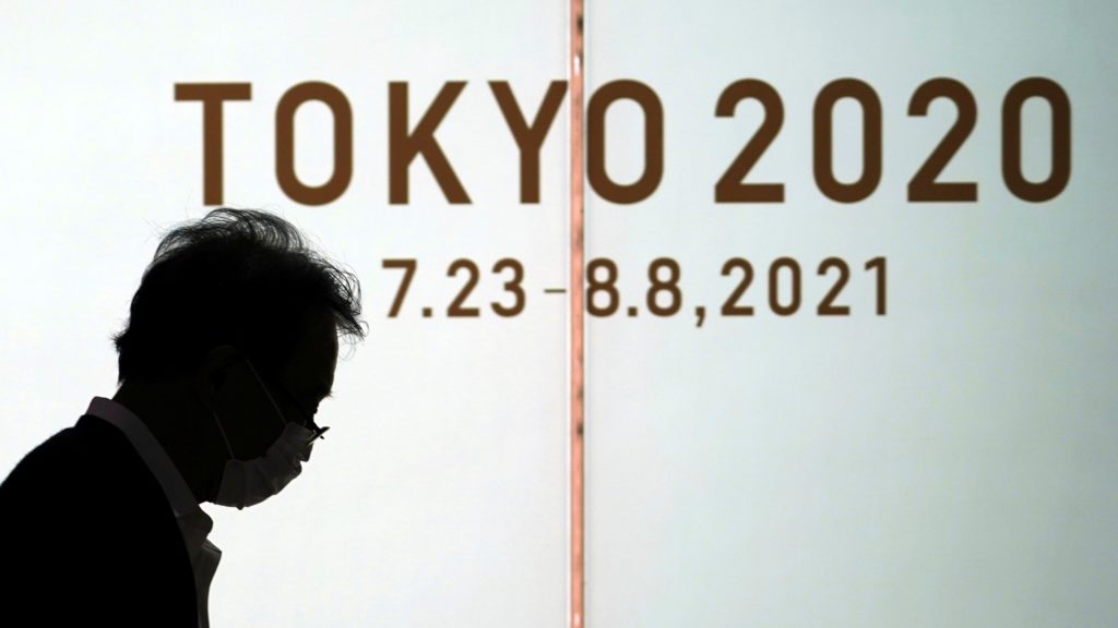Védőmaszkos férfi megy a tokiói nyári olimpiát hirdető plakát előtt a japán fővárosban