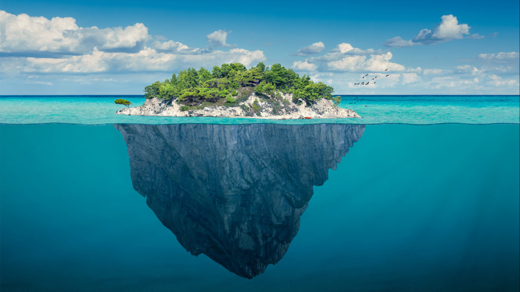 Beautiful underwater view of lone small island above and below the water surface in turquoise waters of tropical ocean.