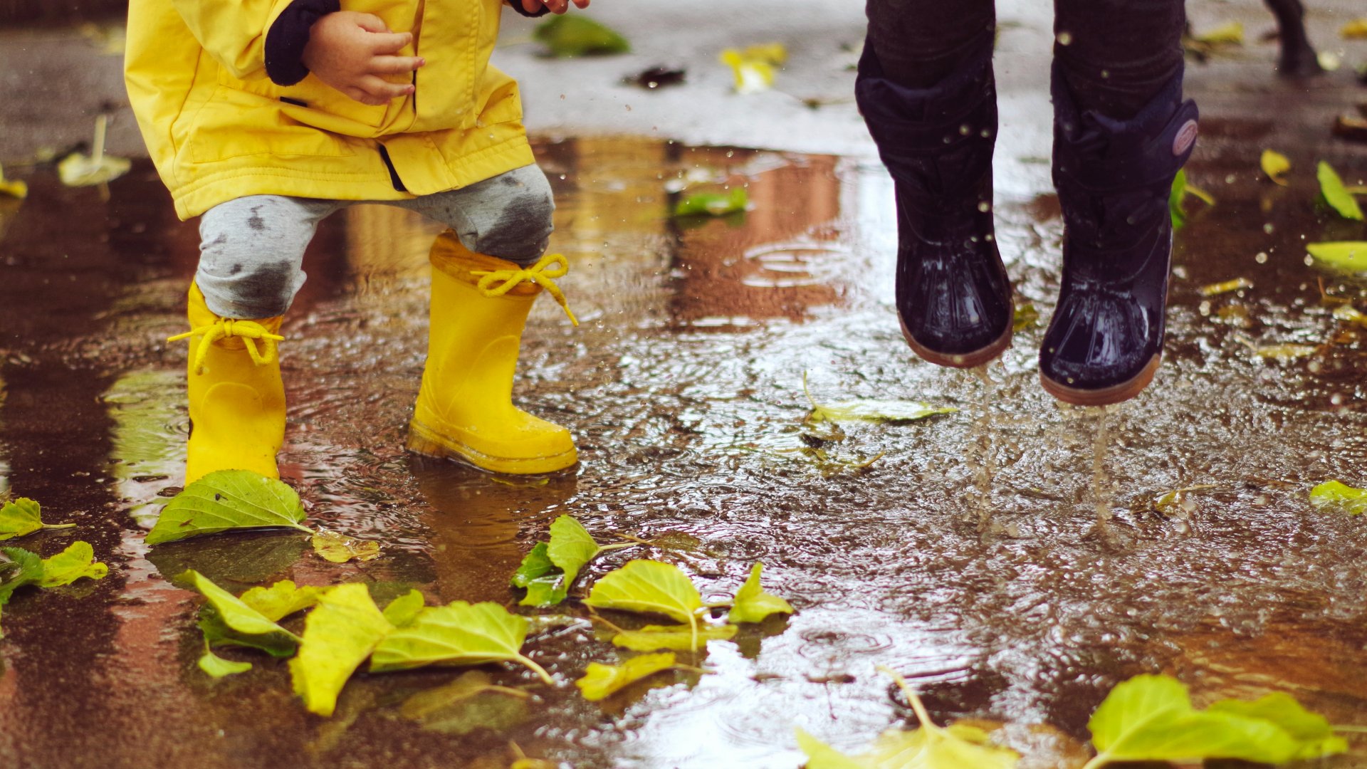 Gyerekek ugrálnak gumicsizmában a pocsolyákba az őszi esős időben