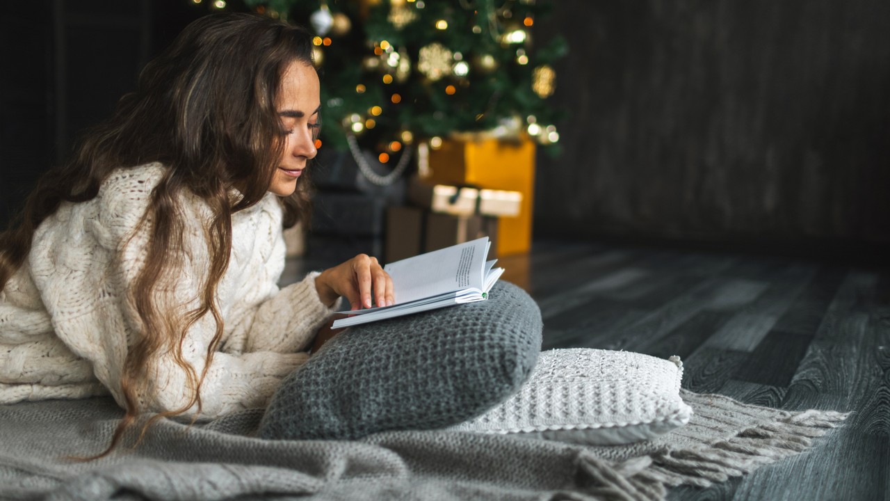 Könyvet olvasó nő a karácsonyfa mellett