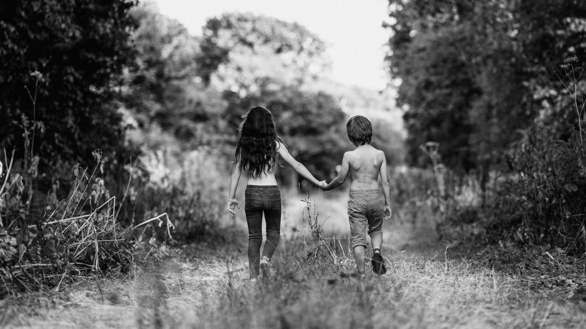 Egy kislány és egy kisfiú kézenfogva sétál az erdőben