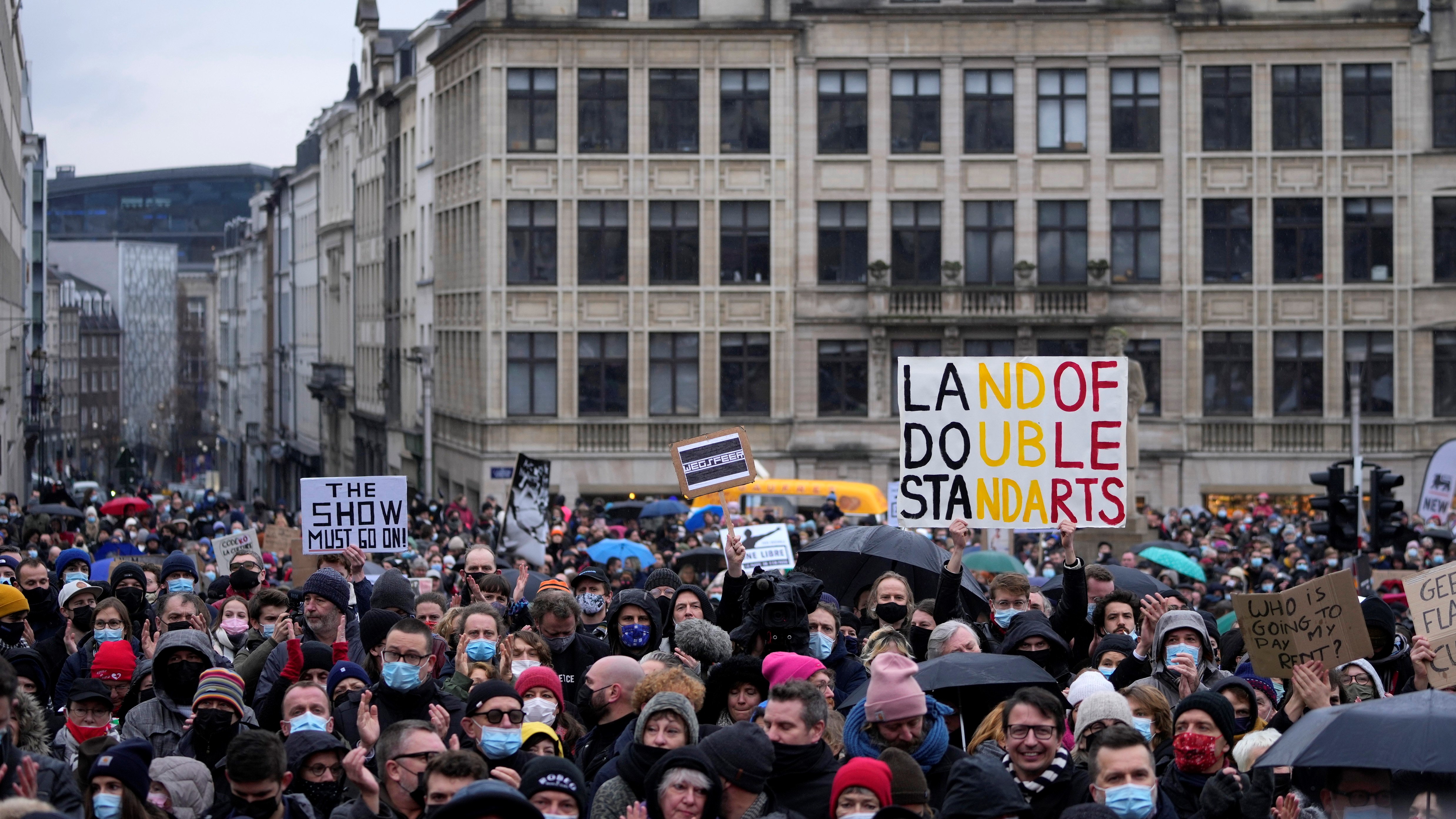 Előadóművészek, rendezvényszervezők, mozitulajdonosok és mások tüntetnek a koronavírus omikron variánsának terjedésének korlátozása céljából bevezetett, főként a kulturális szektort érintő korlátozások ellen Brüsszelben 2021. december 26-án. A kettős mérce országa feliratú táblát tart az egyik tiltakozó. (Fotó: MTI/AP/Virginia Mayo)