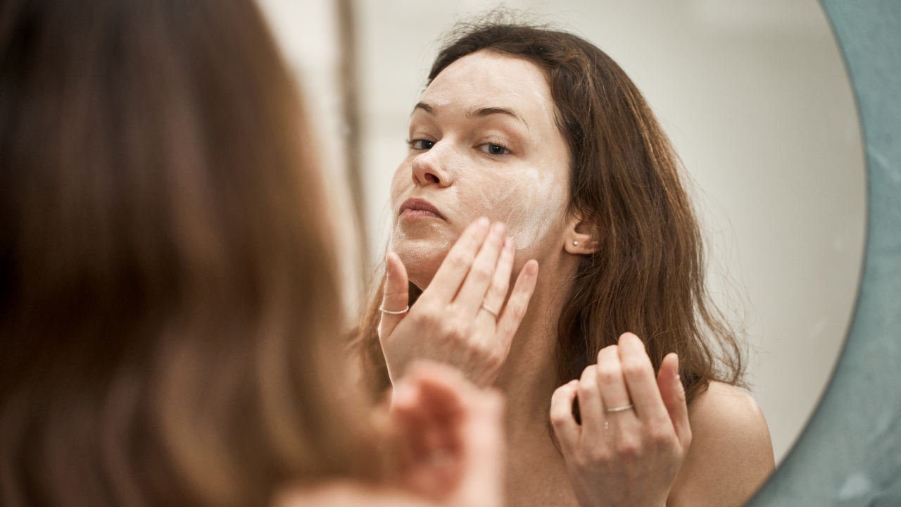 Fiatal nő arcára krémet ken a tükörben
