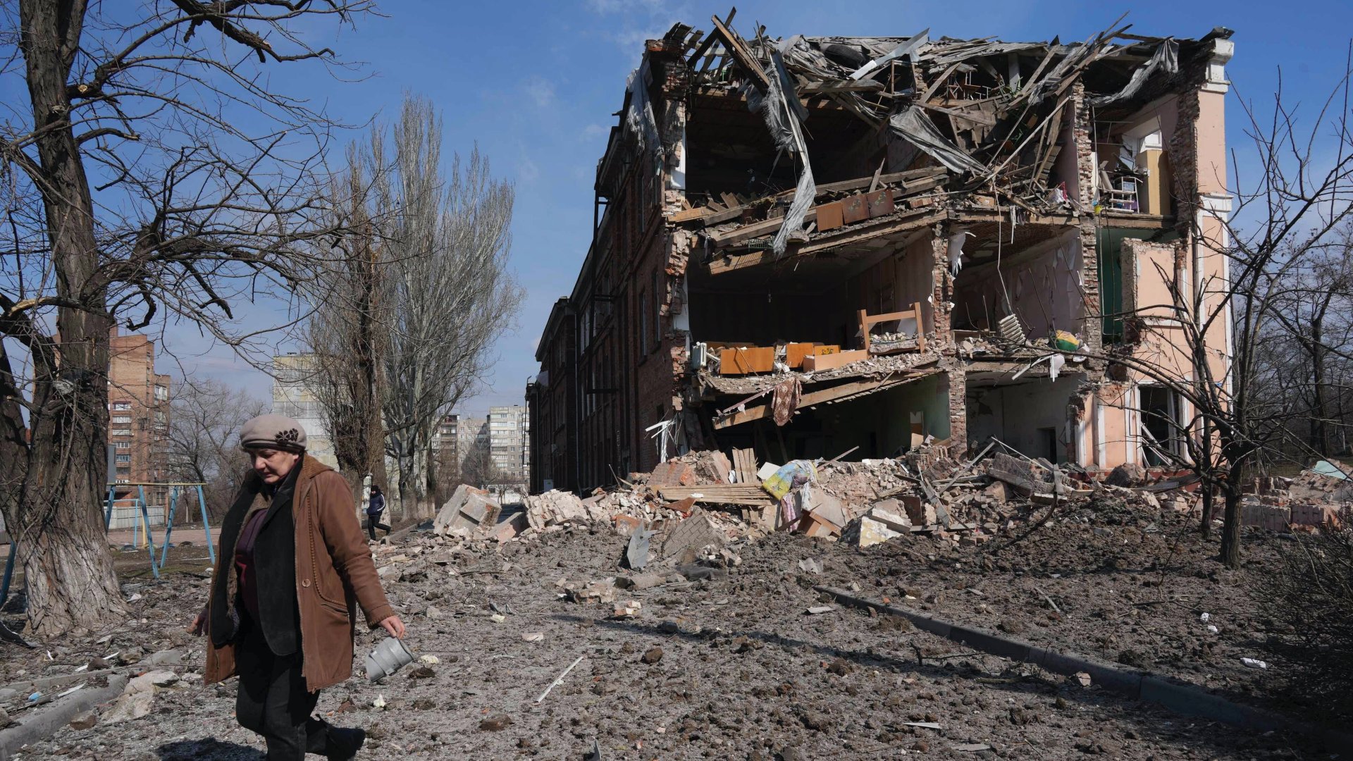 Nõ halad el egy tüzérségi támadásban megrongálódott épület elõtt Mariupolban 2022. március 13-án