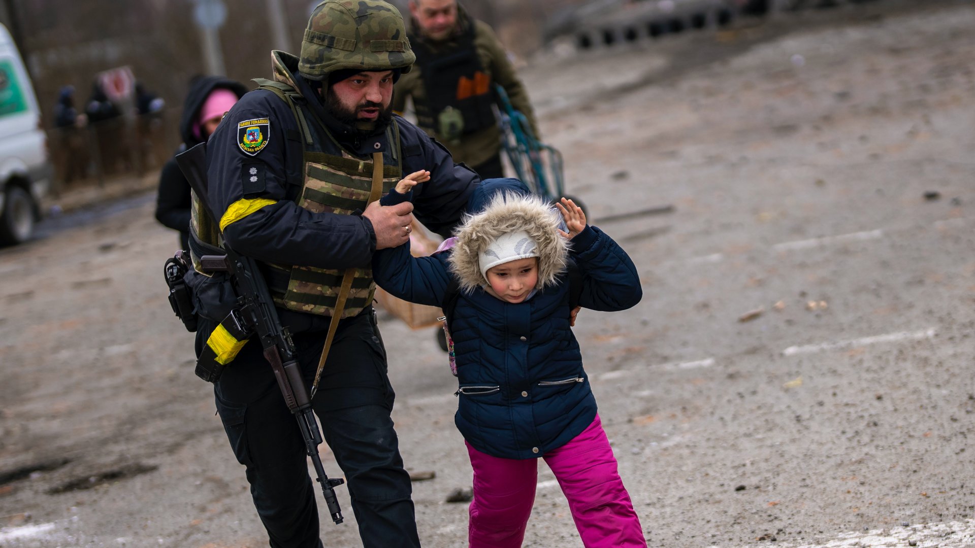 Ukrán rendõr segít egy gyereknek, miközben menekülnek a Kijev közelében lévõ Irpinybõl 2022. március 7-én.