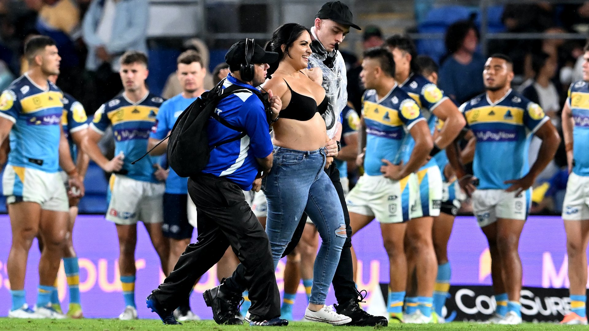 A biztonsági őrök egy beszaladó nőt visznek el a pályáról a Gold Coast Titans és a Parramatta Eels közötti NRL-mérkőzés ötödik fordulójában a Cbus Super Stadiumban, 2022. április 09-én, az ausztráliai Gold Coastban