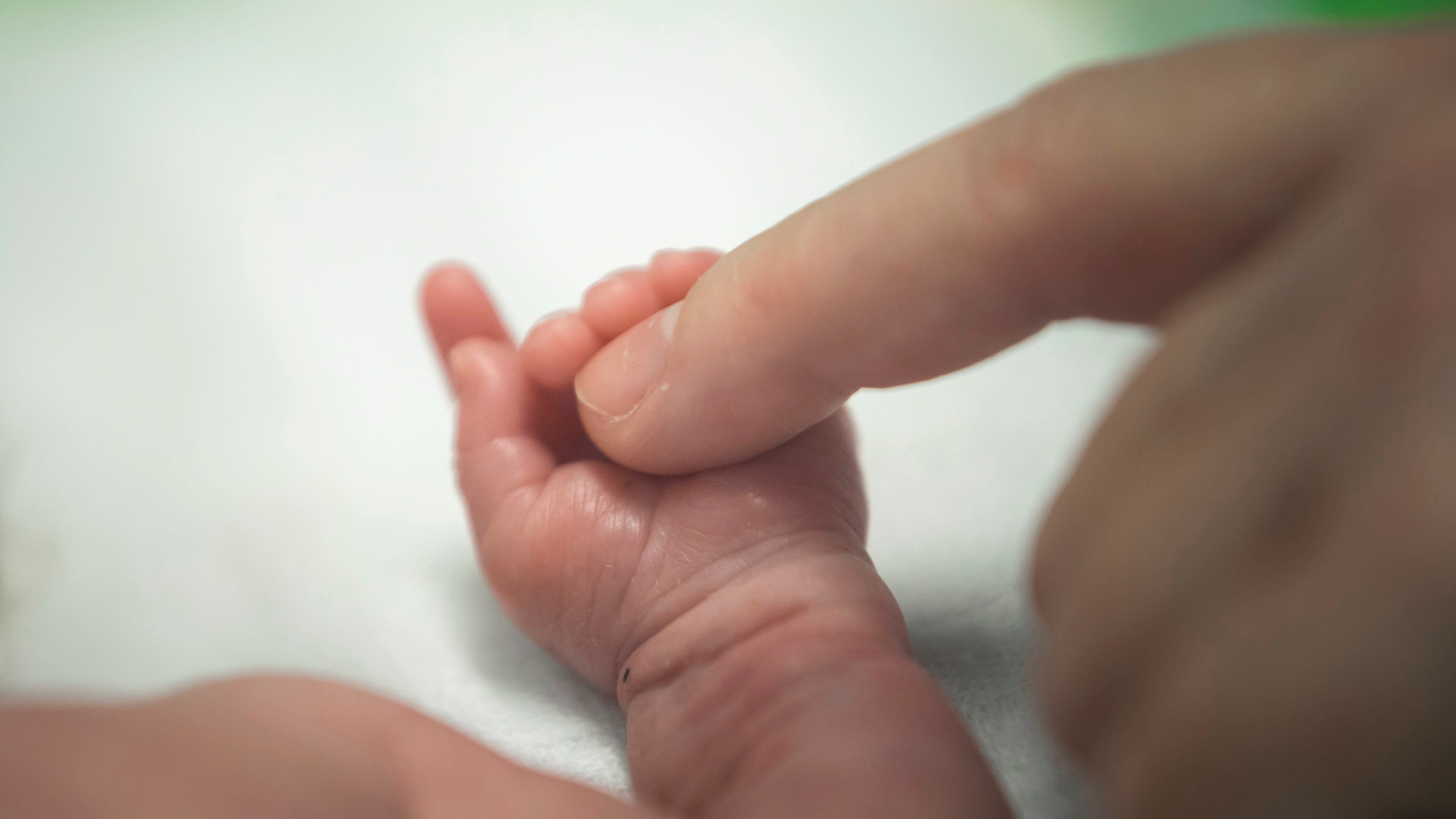 Egy koraszülött kislány kezét érinti ujjával édesanyja