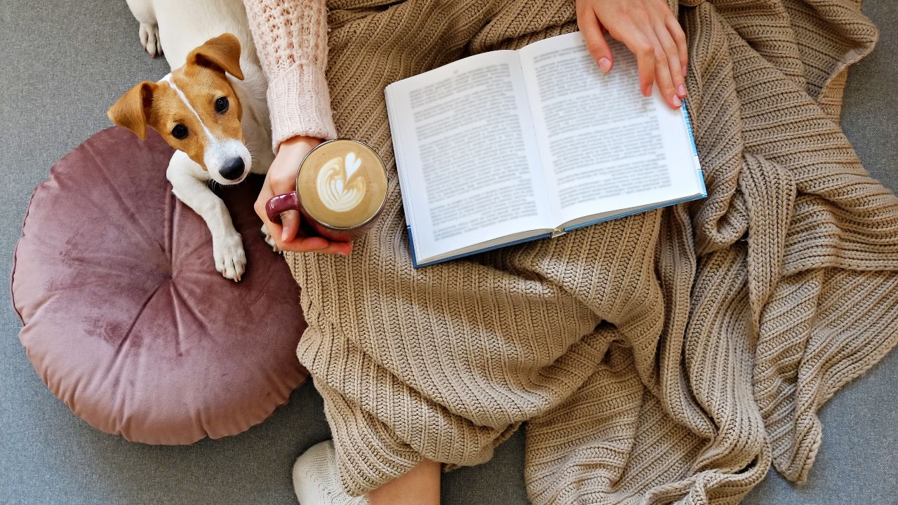 Nő kutyával ül a földön és könyvet olvas