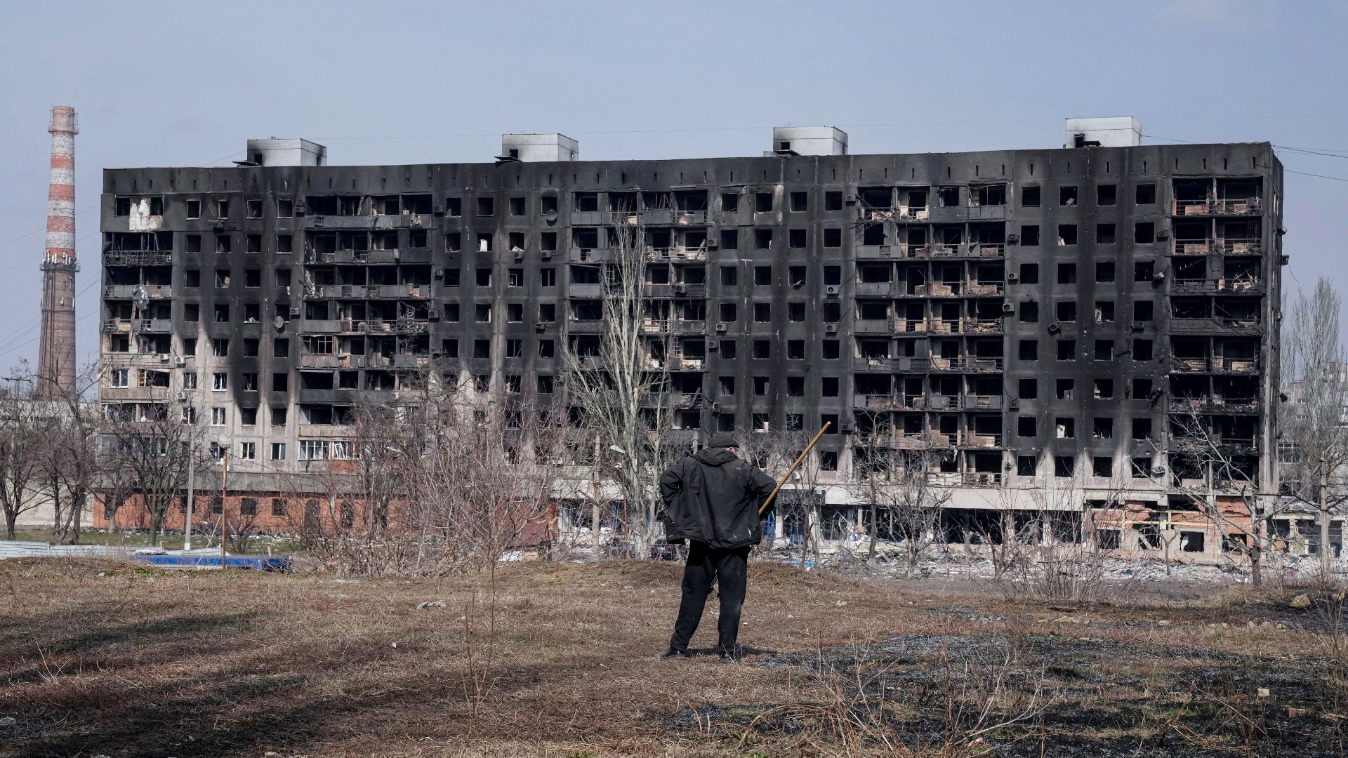 Egy férfi egy romos házat néz Mariupolban