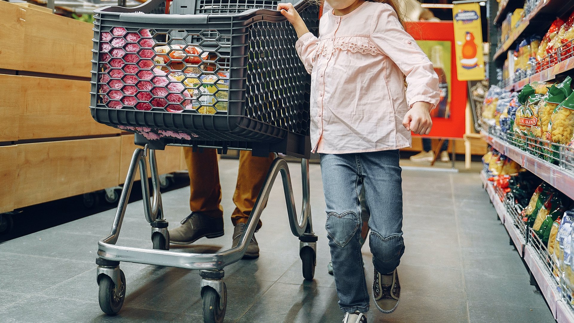 Kislány a családjával egy bevásárlókocsi mellett egy szupermarketben