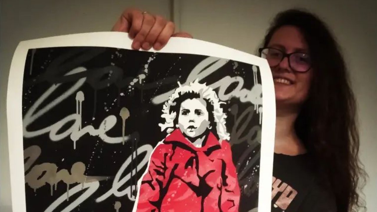 Egy plakátot mutat a piros kabátos kislányról Oliwia Dabrowska, a Schindler listája gyerekszínésze