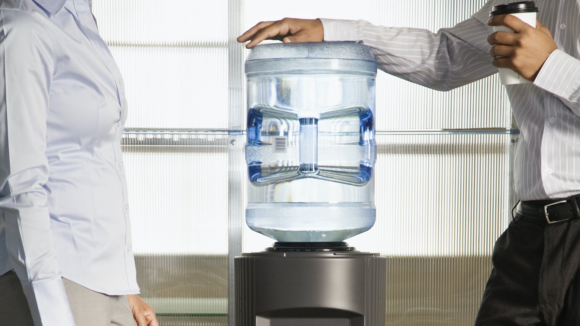 Két irodai dolgozó áll egy vízautomata mellett