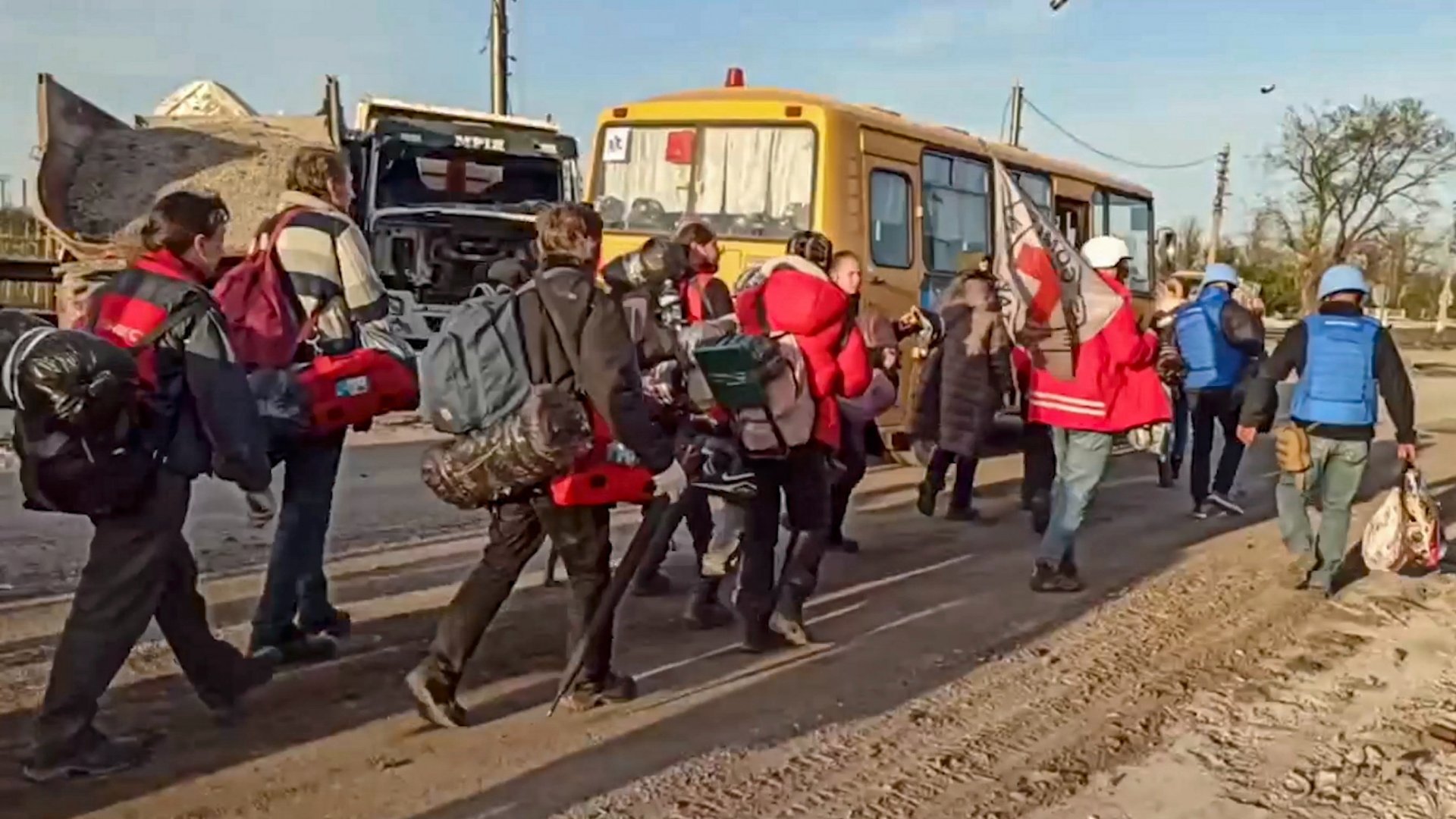 Az orosz védelmi minisztérium által közreadott, videóról készült képen orosz katonák és vöröskeresztes aktivisták kísérik buszokhoz az Azovsztal acélmûbõl kimenekített civileket Mariupolban 2022. május 6-án