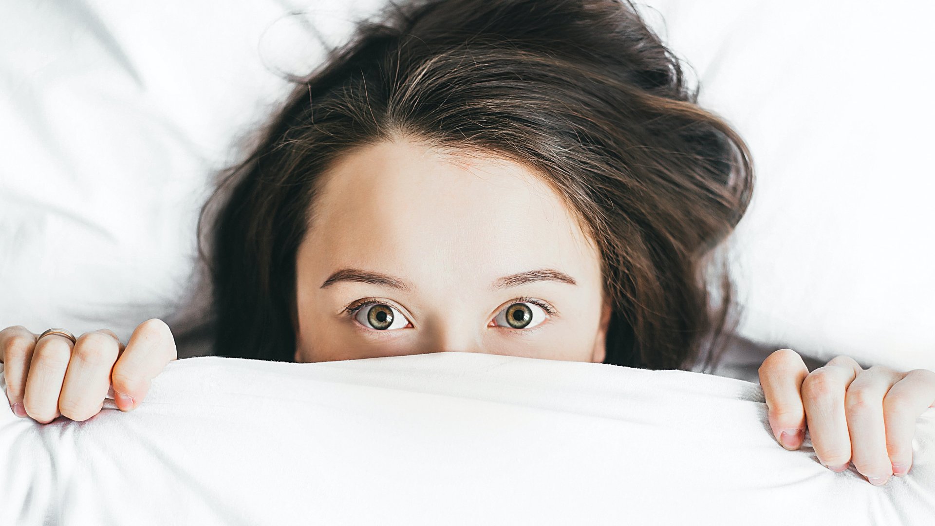 Egy ágyban fekvő nő kinéz a takaró alól