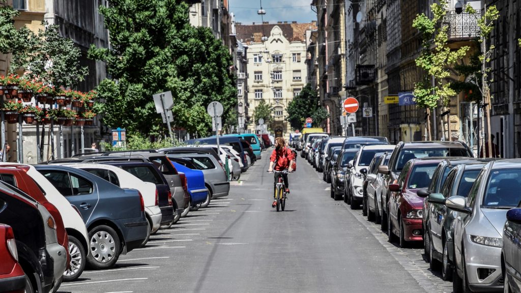 Kerékpáros közlekedik Budapesten a kétoldalt parkoló autók között