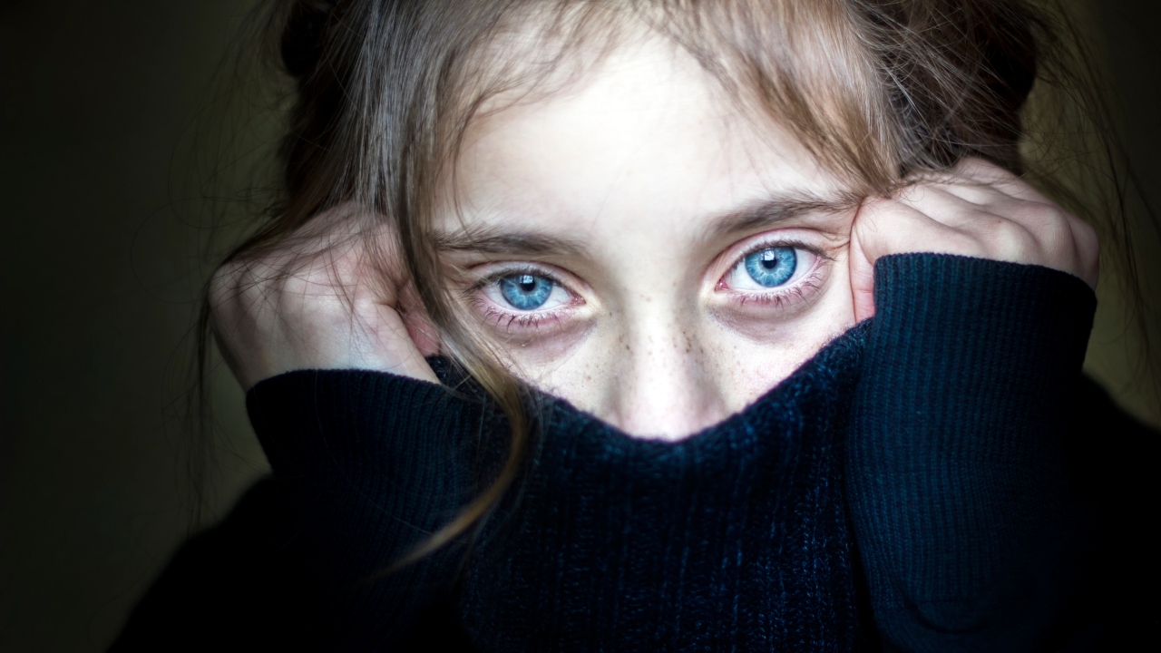 Kék szemű fiatal lány arcát félig eltakaró fekete garbóban
