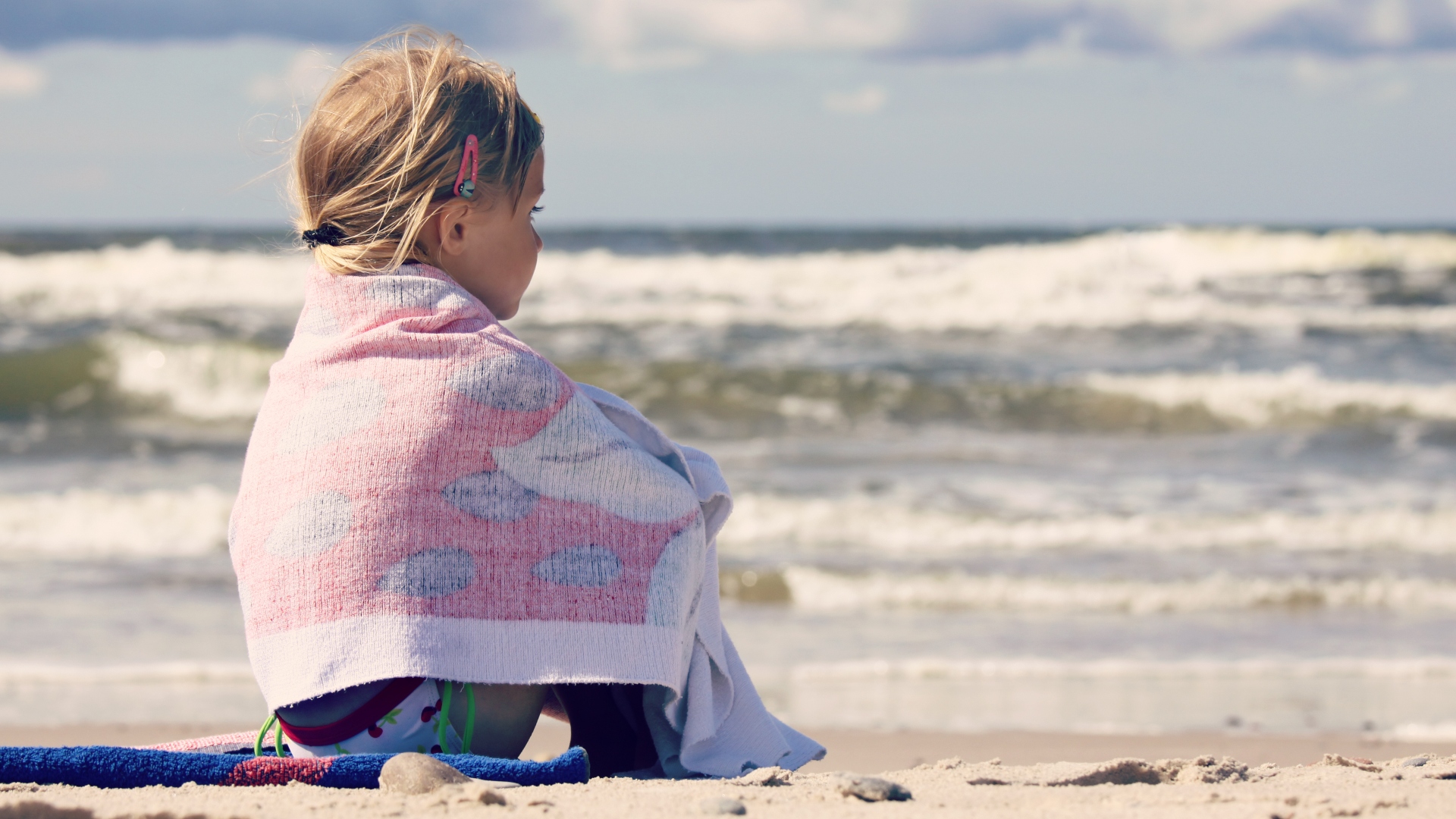 Kislány ül törülközőbe csavarva a strandon