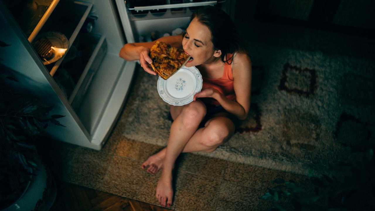 Fiatal nő pizzát eszik a földön ülve