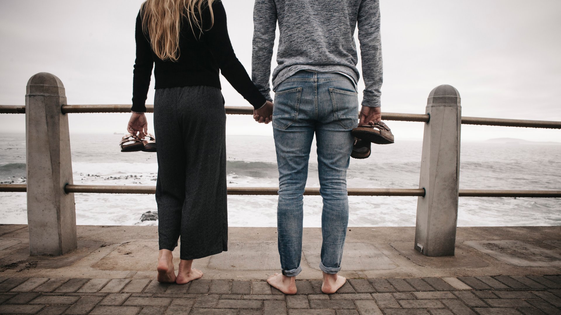 Fiatal pár a tengerparton kézenfogva ruhában, mezítláb