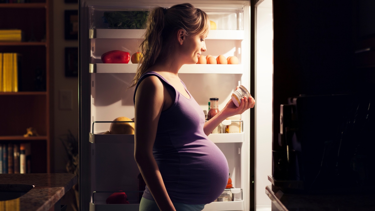 Terhes kismama áll a hűtő előtt