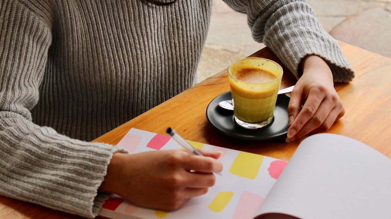 Nő ír egy mappába, kávéval a kezében