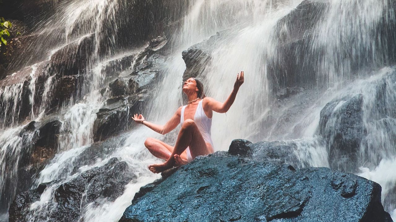 Nő ül egy sziklán a vízesés alatt