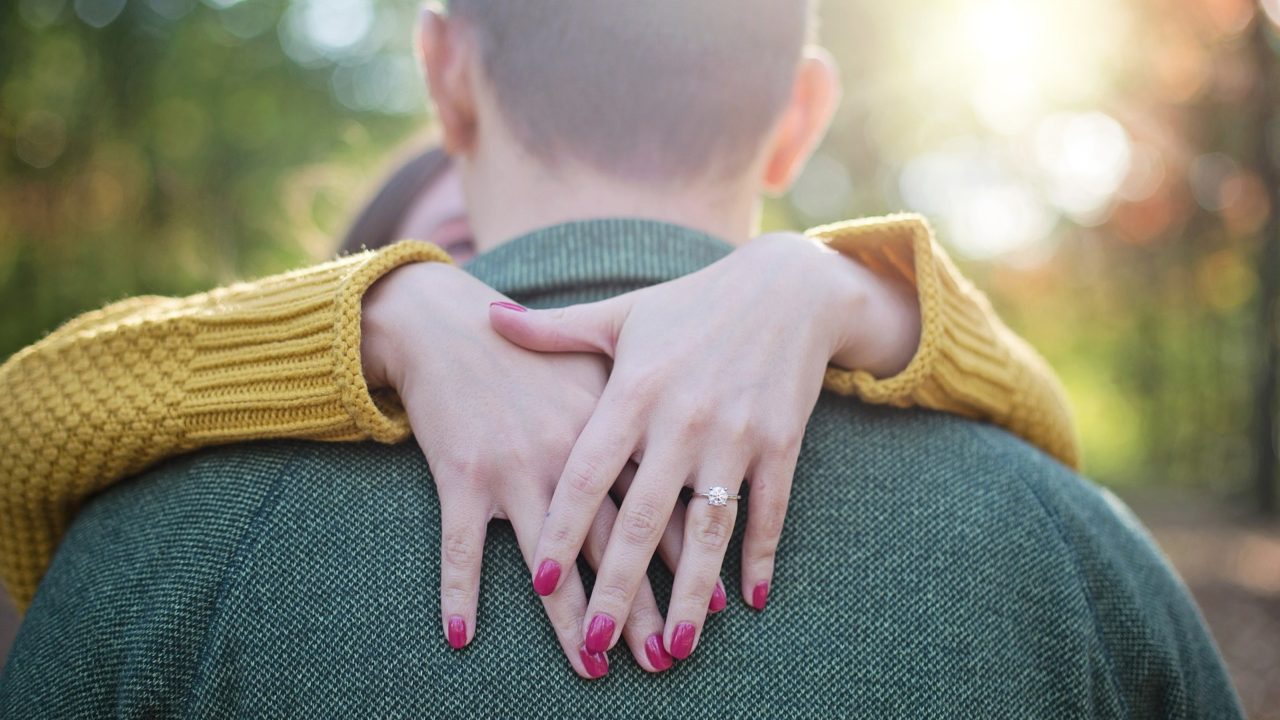 Férfi nyakát átölelő nő eljegyzési gyűrűvel az ujján.