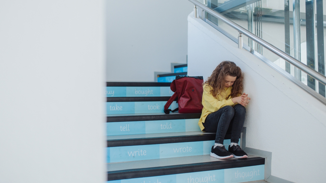 Szomorú kislány ül az iskolában a lépcsőn