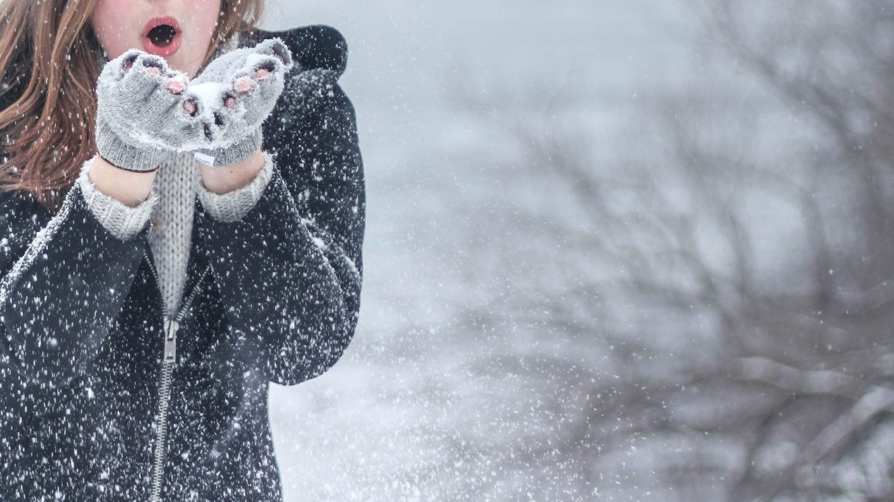 A tenyeréből havat fújó fiatal nő egy téli tájon.