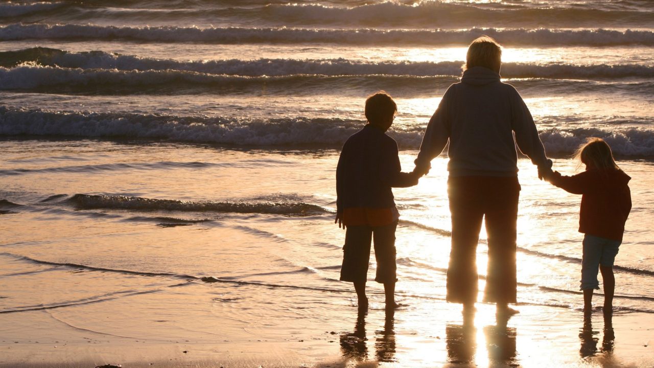 Anya fogja fia és lánya kezét. Háttal állnak a kamerának a tengerparton, ahol a lemenő nap fénye mindent aranyszínűre fest.