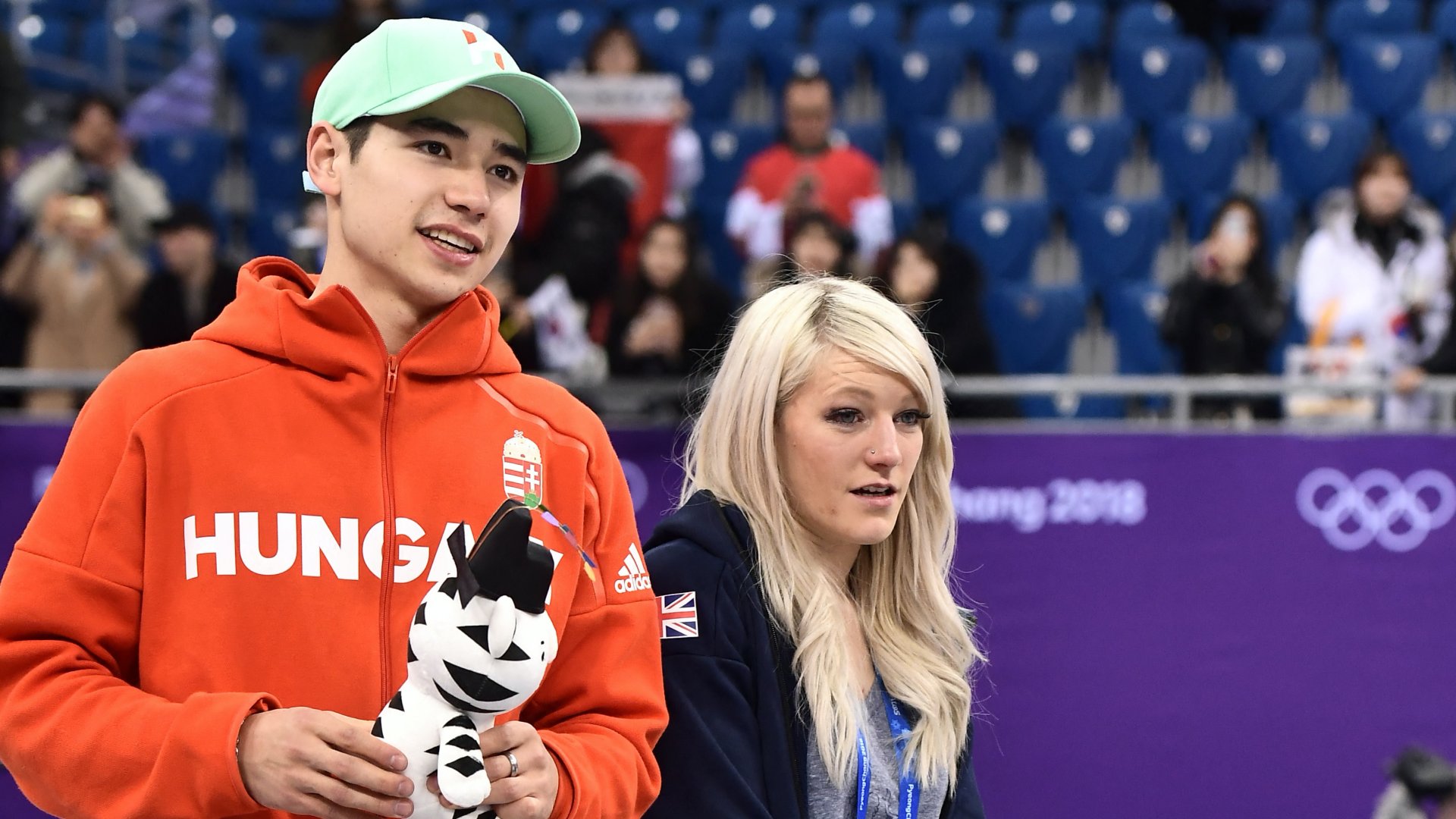 Liu Shaolin Sándor a brit Elise Christie mellett áll a férfi 5000 méteres váltó rövidpályás gyorskorcsolya versenyszámának helyszínén rendezett ünnepségen a 2018-as pjongcsangi téli olimpiai játékok helyszínén, a Gangneung Jégarénában 2018. február 22-én