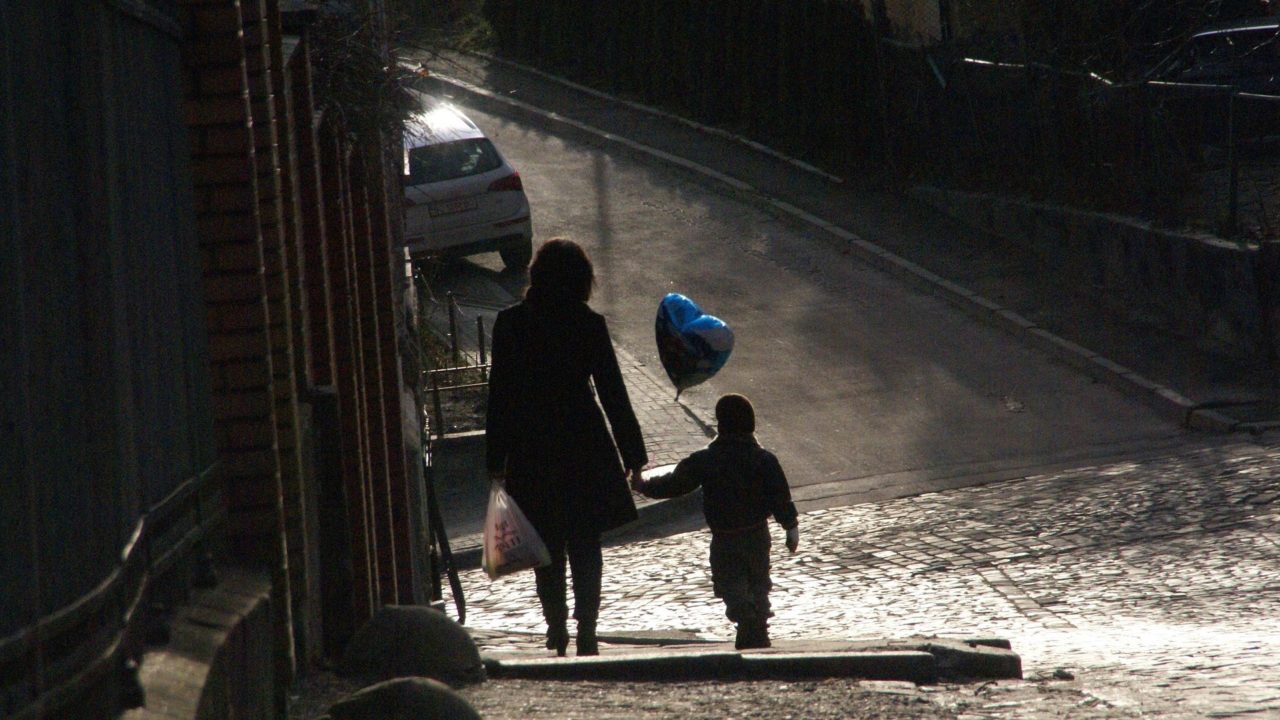 Anya sétűl a fiával. A fiú kezében egy kék, szív alakú lufi zsinórja van.