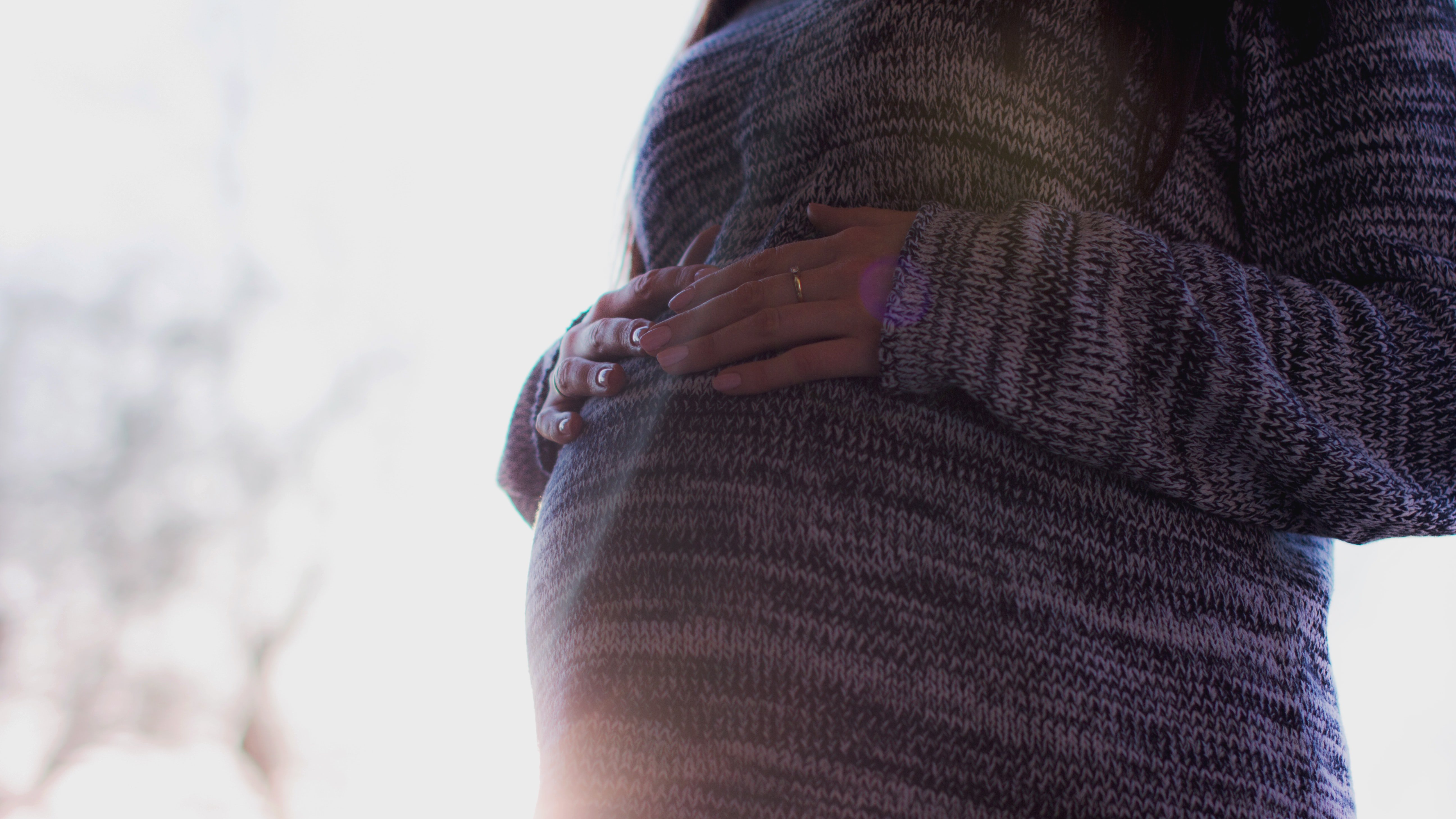Terhes nő pulóverben a hasára teszi a kezét
