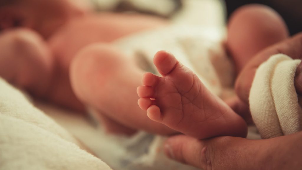Egy újszülött csecsemő talpa egy felnőtt ujjai között
