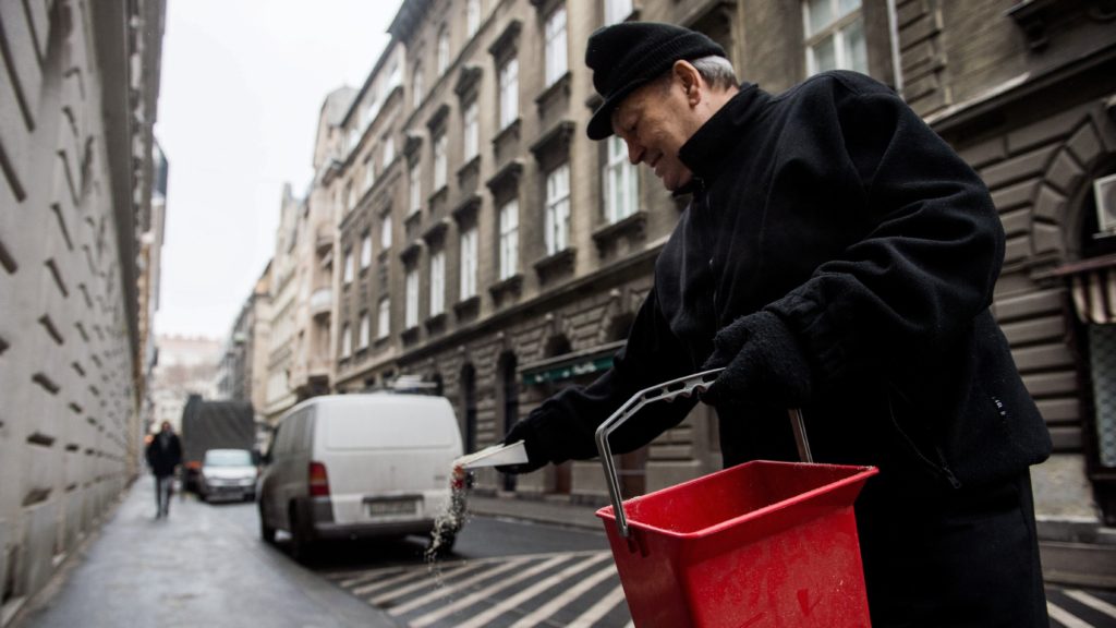 Csúszásgátló anyagot szór egy férfi a járdára Budapest belvárosában. 