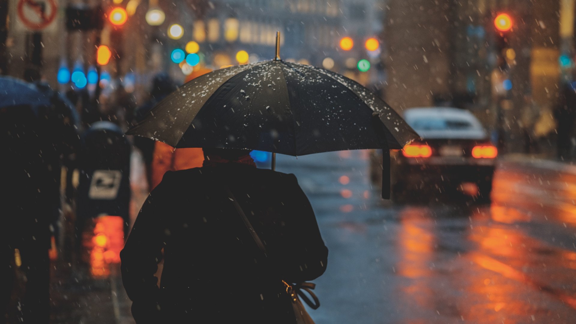 Esernyővel sétáló ember a városban enyhe havazásban