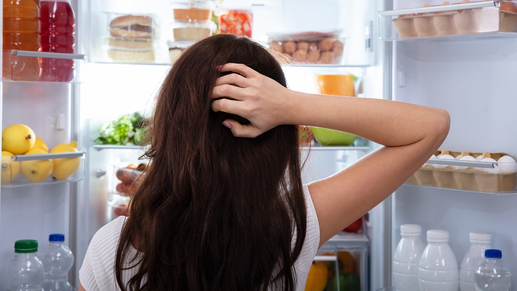 Tanácstalan nő áll a hűtő előtt