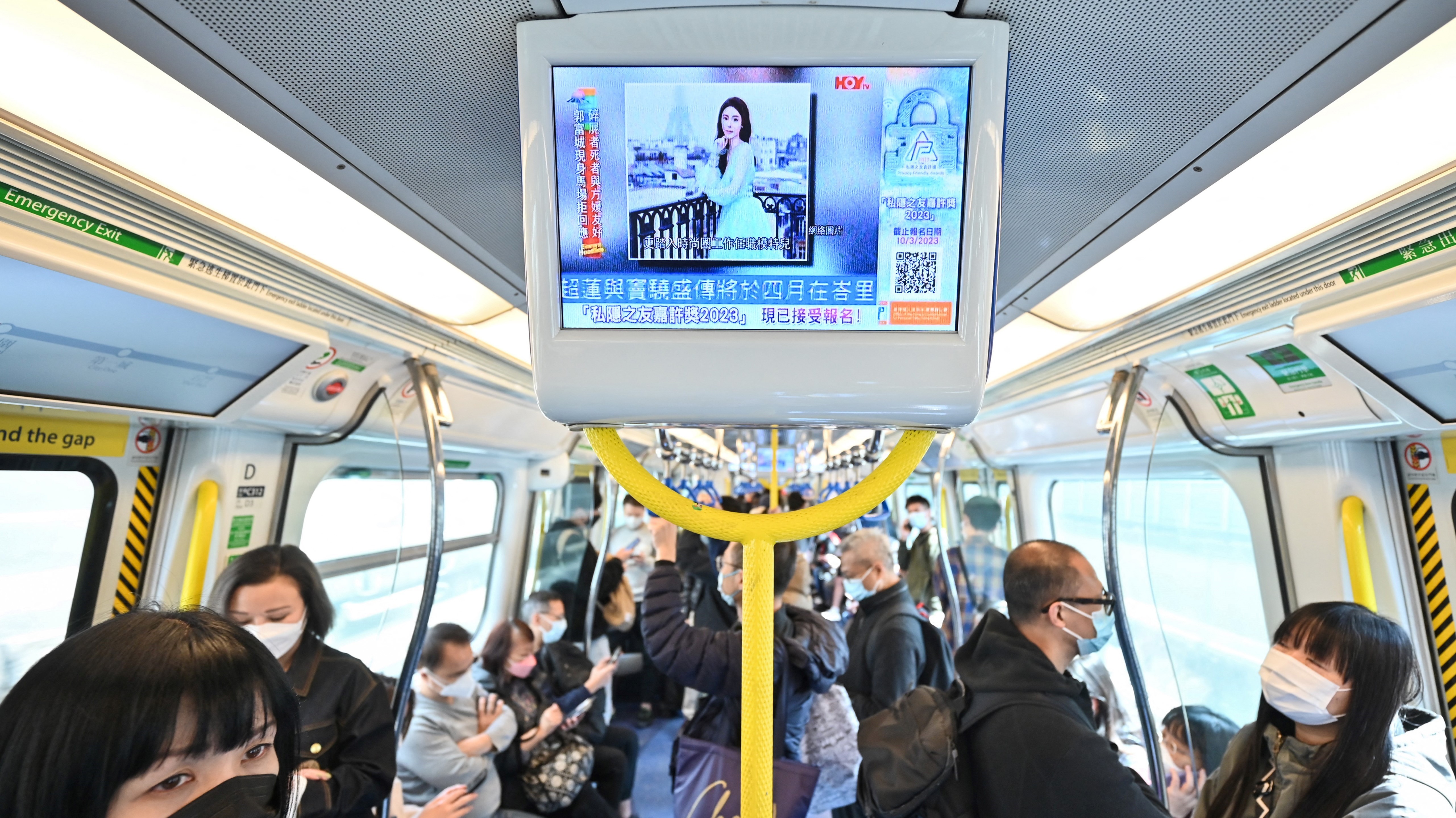 Vonaton utazó emberek nézik az Abby Choi-ról szóló híreket 2023. február 27-én Hongkongban. 
