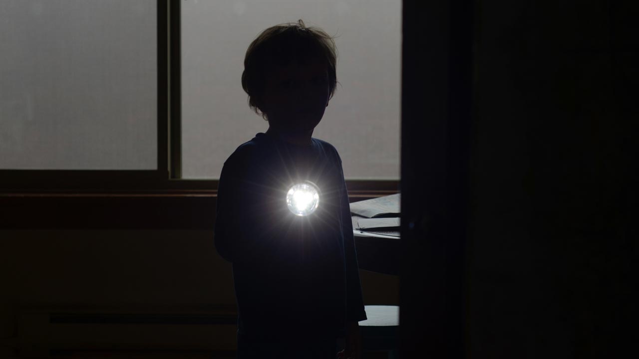Zsemlámpával világít egy kisfiú a sötétben