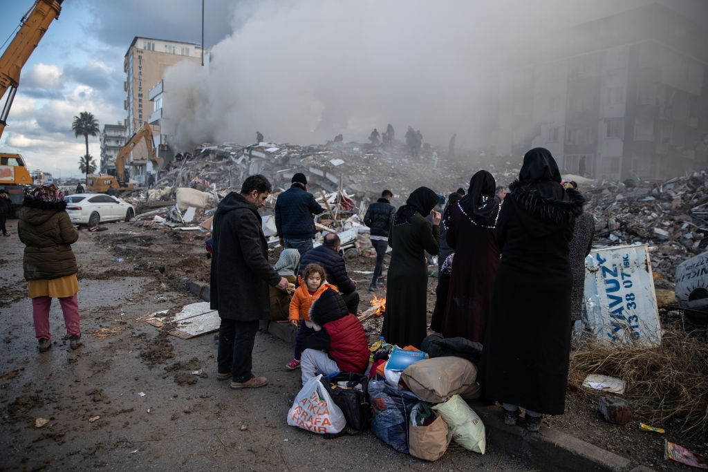 A földrengés túlélői várakoznak a járdán egy ház romjai mellett.