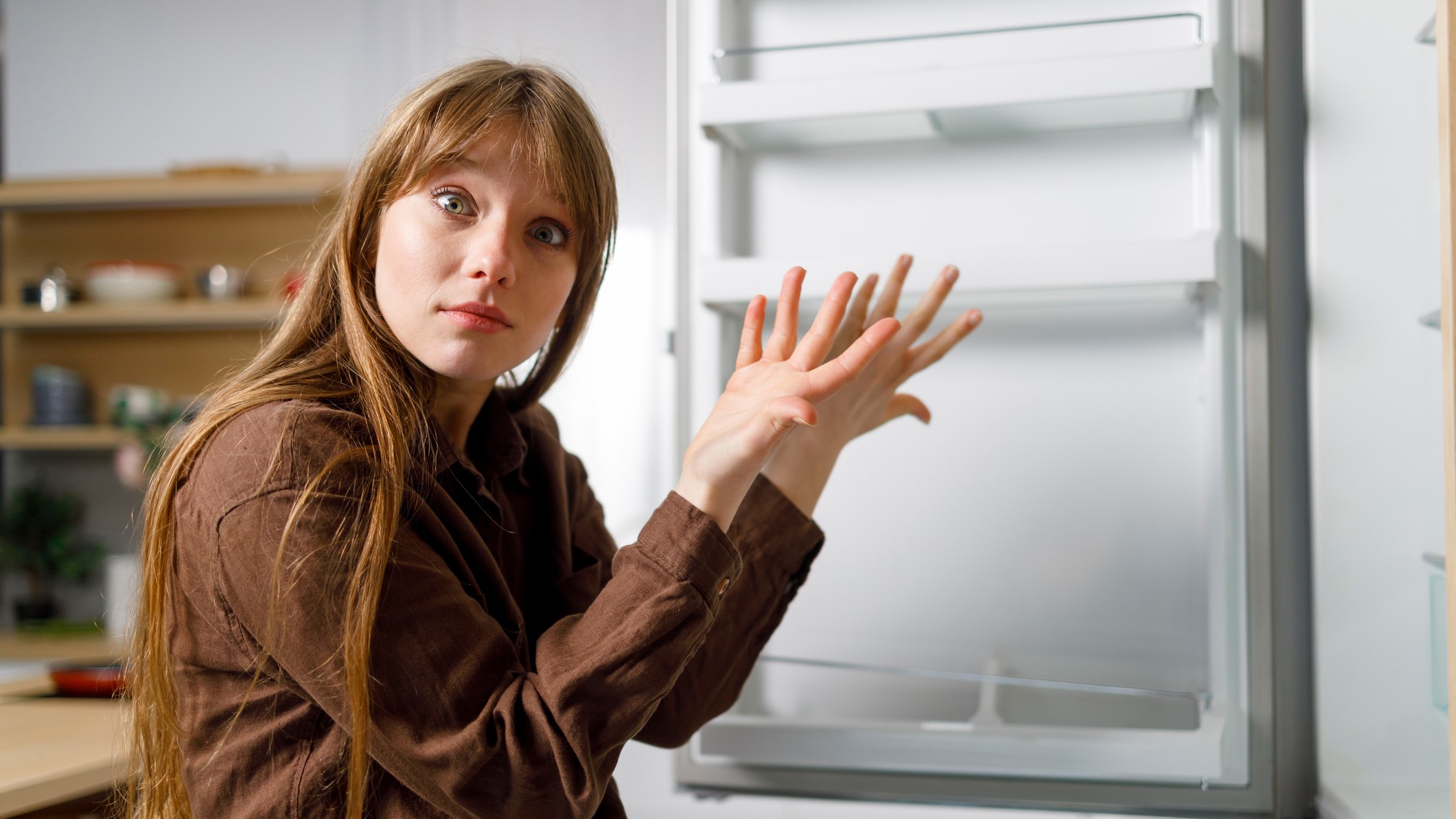 Fiatal nő tanácstalanul áll a hűtő előtt