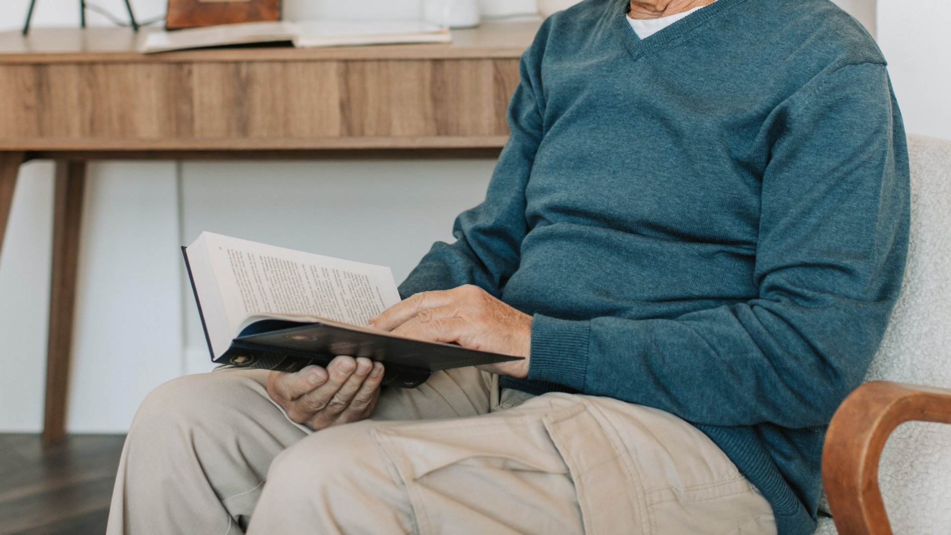 Idős férfi könyvet olvas egy fotelben ülve