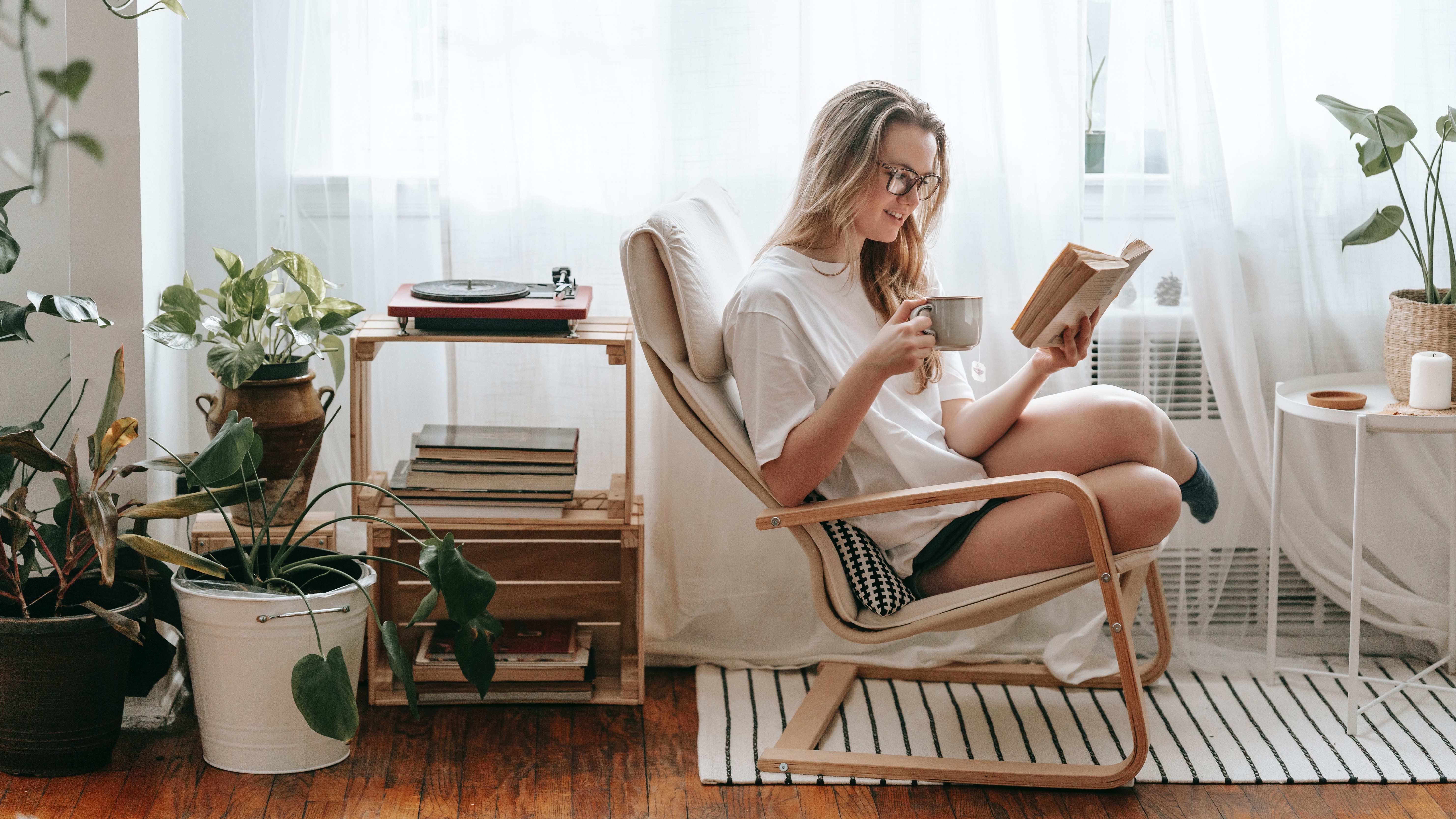 Fiatal nő egy székben olvas és kávézik