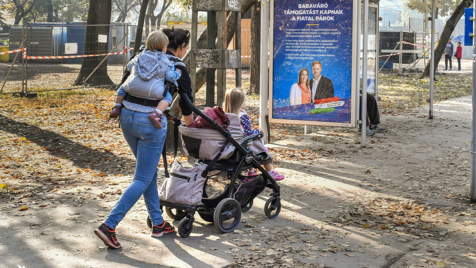 Egy fiatal anya germekeivel sétál egy babaváró támogatást hirdetõ plakát mellett a Városligetben