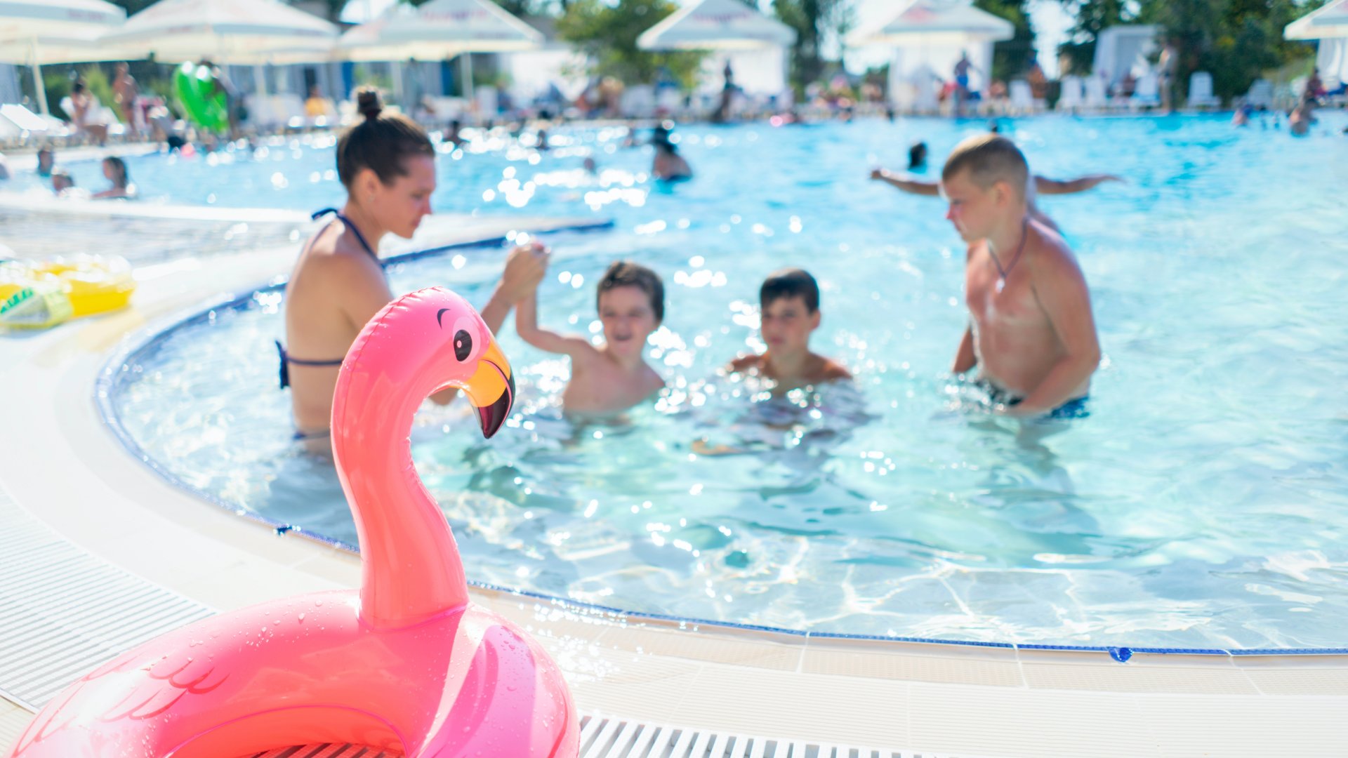 Gyerekek a medencében előtérben egy felfújható rózsaszín flamingó