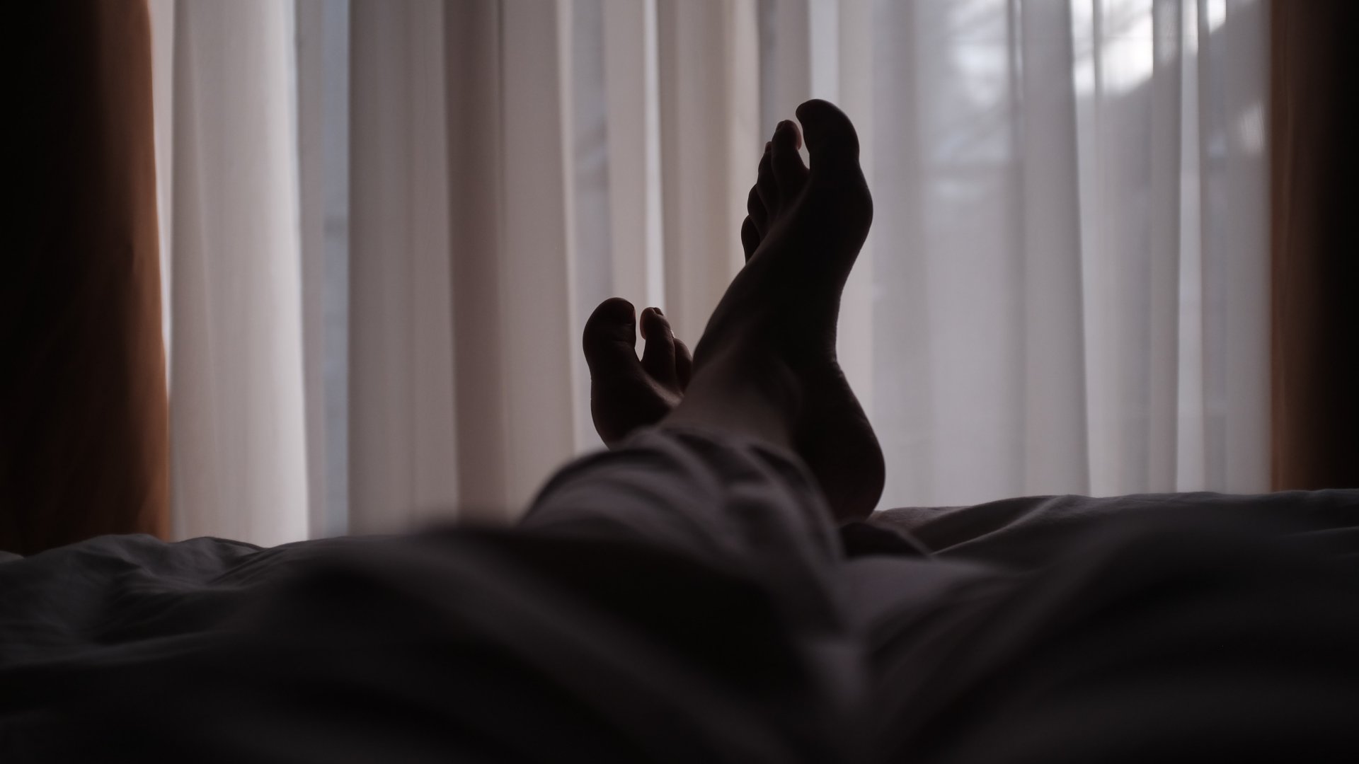 Ágyon fekvő ember keresztbe tett lábai