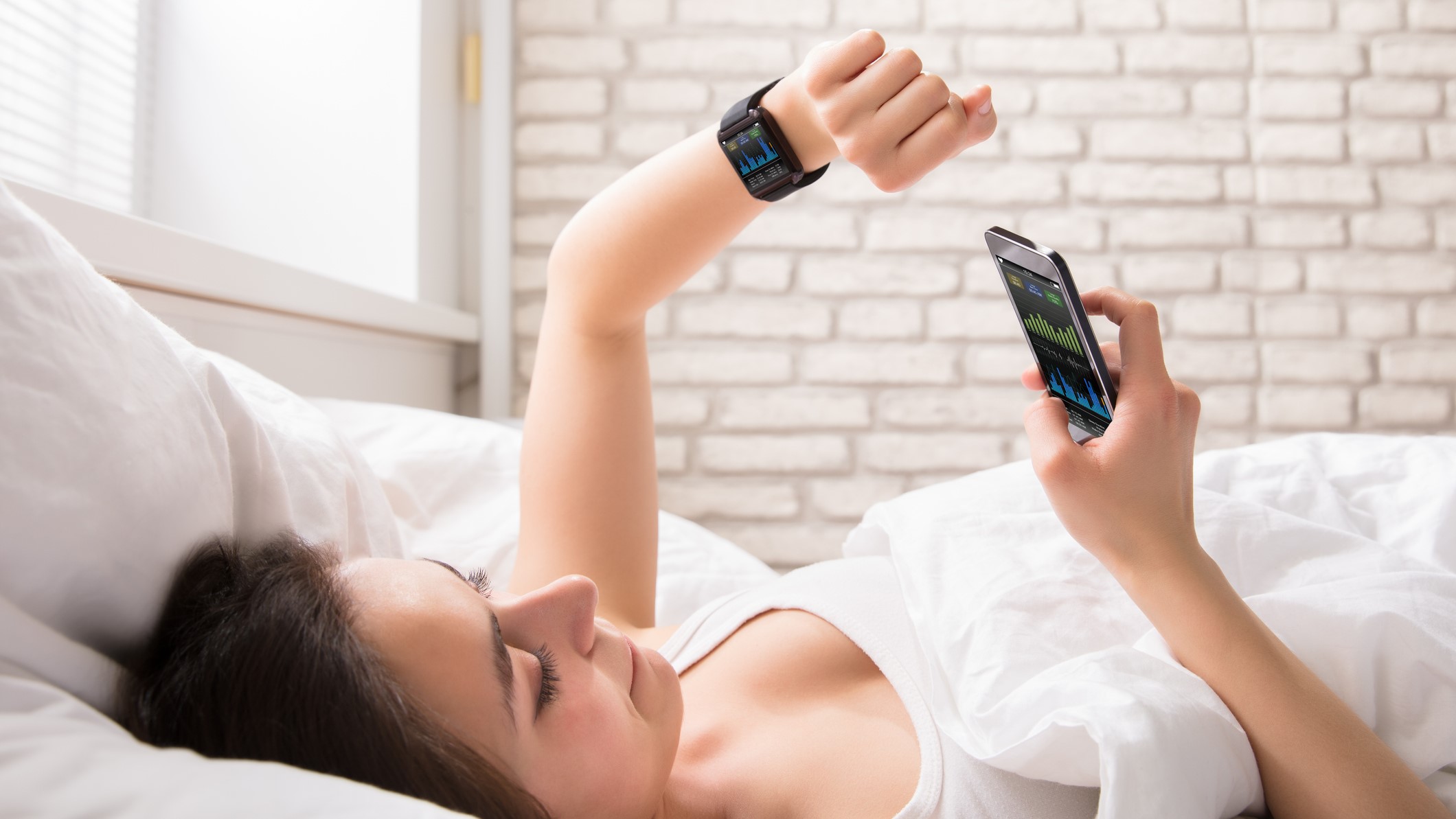 Fiatal nő az ágyon az okostelefonjával és -órájával