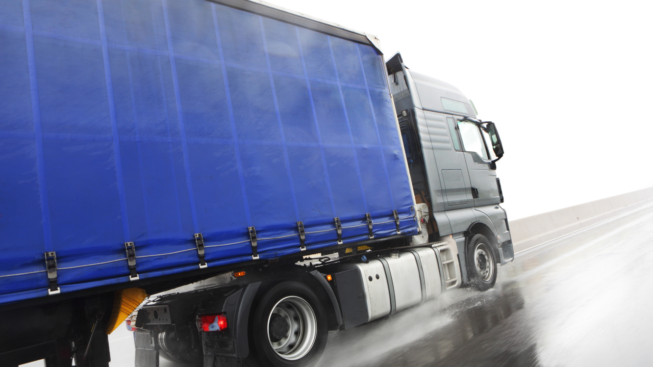 Egy kék teherautó az esős időben halad az autópályán